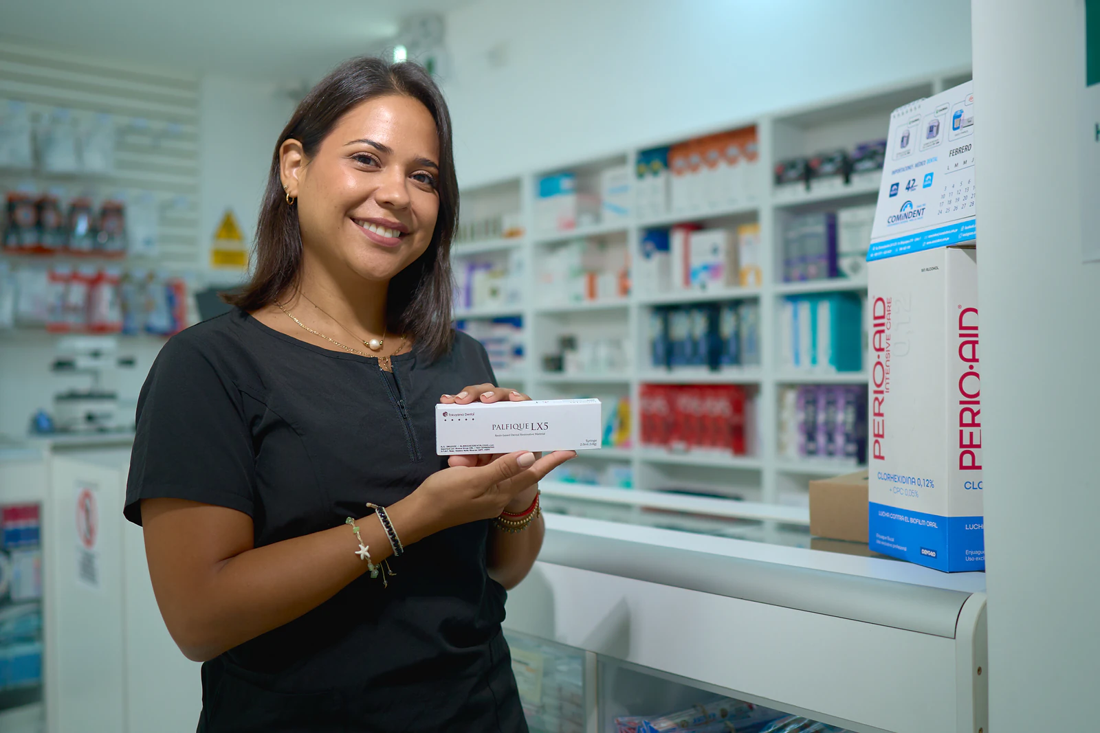 Colaboradora sosteniendo una caja de producto (Palfique LX5) frente a una estantería llena (Perio-Aid y más)